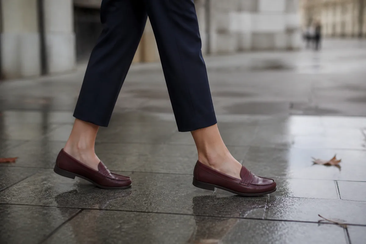 Mocassins plats en cuir bordeaux et pantalon sept-huitièmes sur un trottoir pavé humide