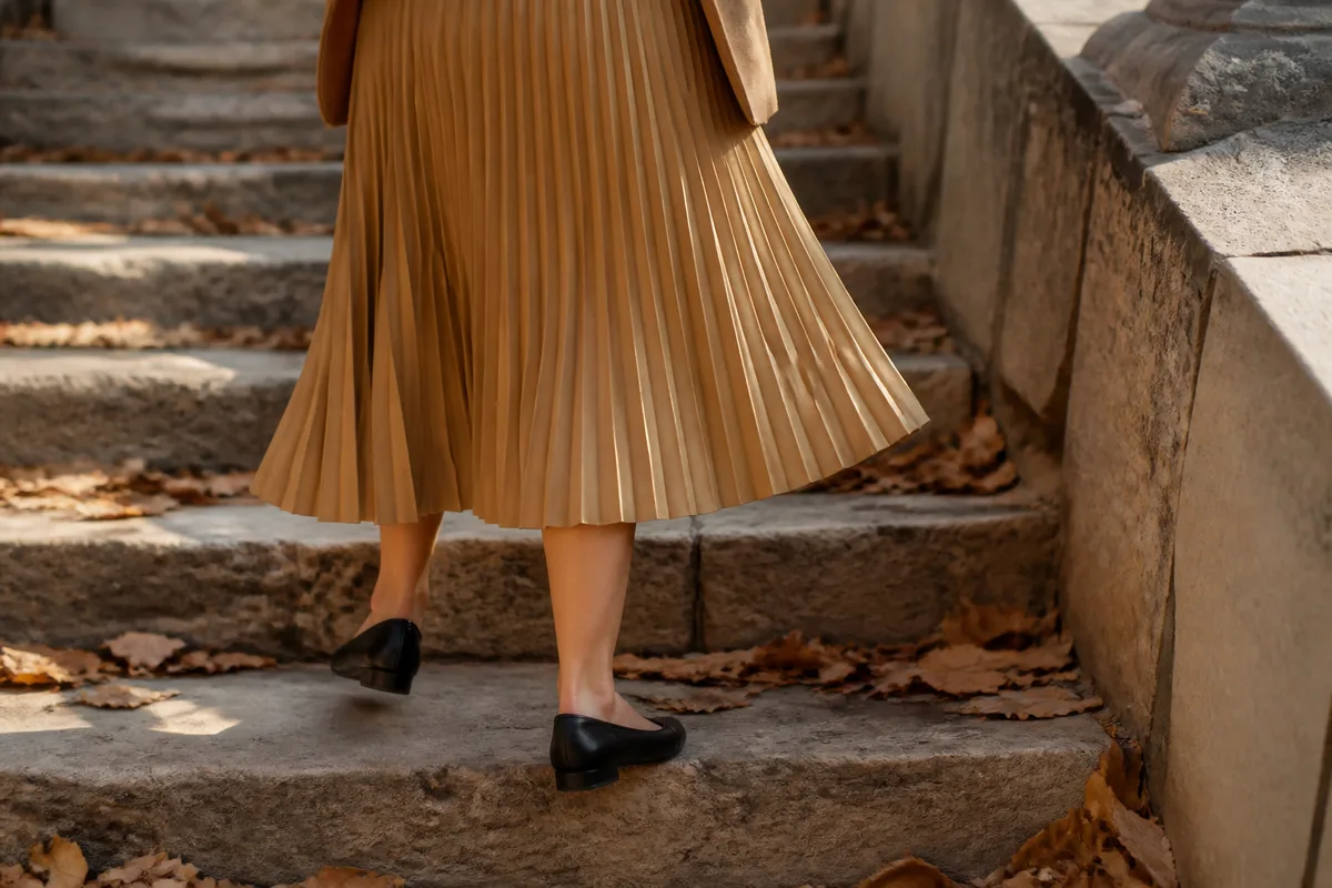 Jupe midi plissée camel et chaussures plates fermées noires dans un escalier de pierre